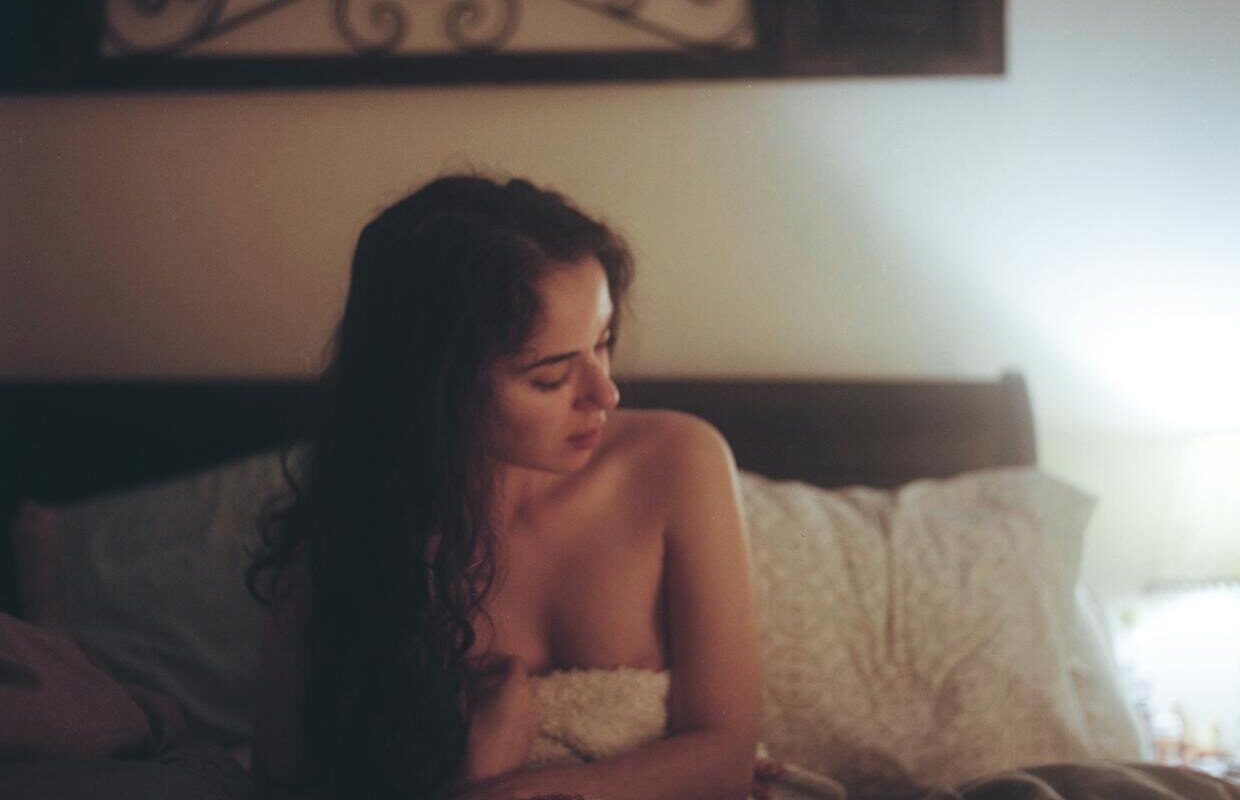 Topless Woman With White and Red Blanket on Bed With Pillows Under Brown Frame Inside White Painted Room